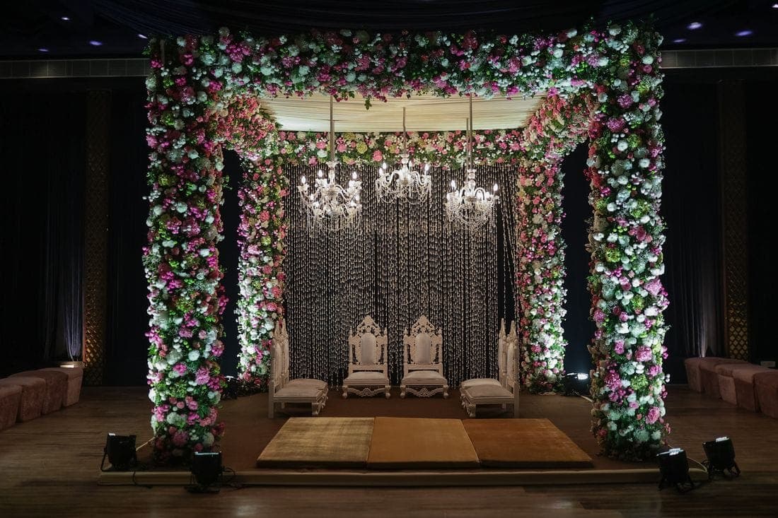 Floral wedding stage with chandeliers and a draped backdrop, set for a barat