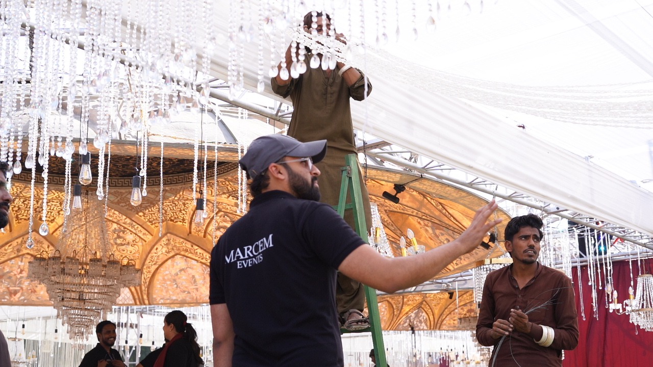 Marcem Events team members hanging crystal chandeliers and fabric draping inside a wedding marquee